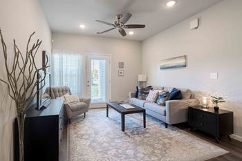 A living room with a grey couch, a black side table, and a ceiling fan.